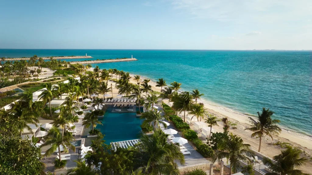 Aerial view of SLS Playa Mujeres resort with infinity pool surrounded by palm trees, white beach, and turquoise Caribbean Sea
